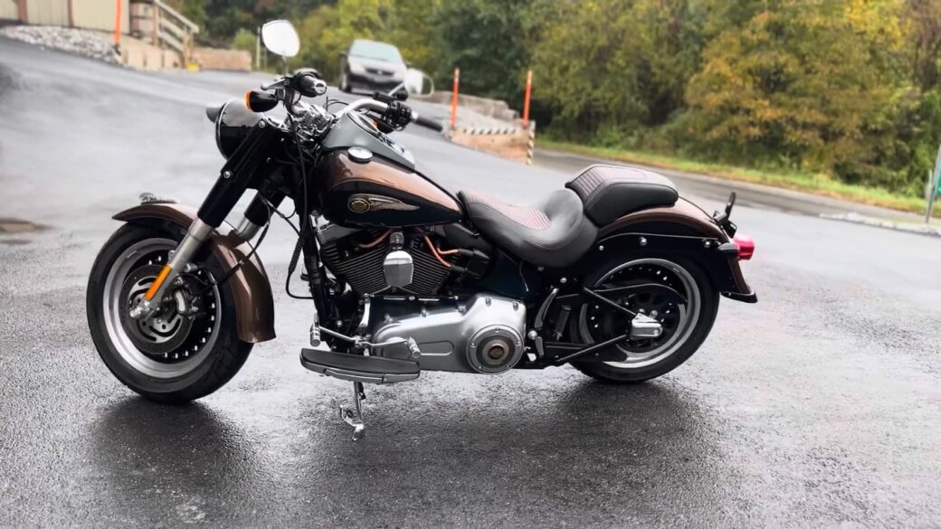 A sleek black motorcycle with chrome accents parked on a wet road, surrounded by trees with a hint of fall colors.